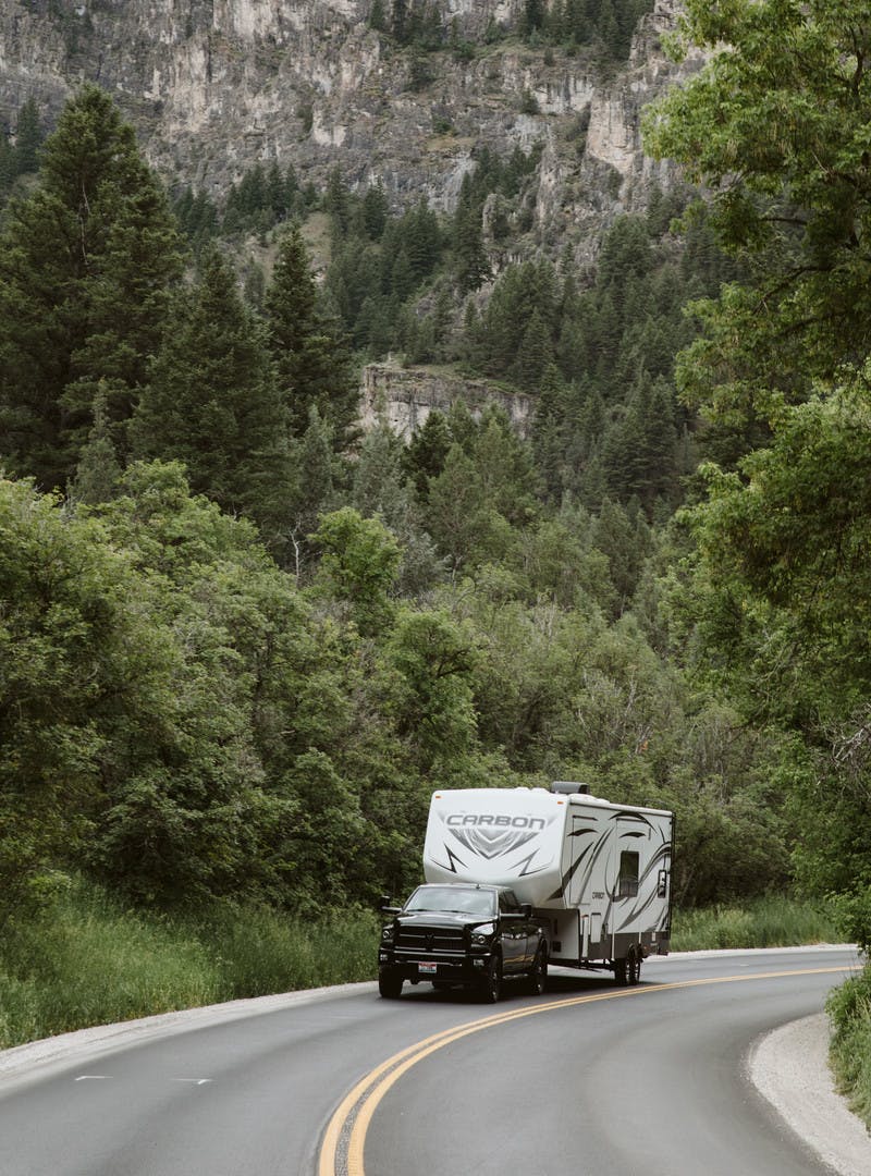 Driving shot of Toy Hauler RV being towed by a truck on the road with mountains in the back.