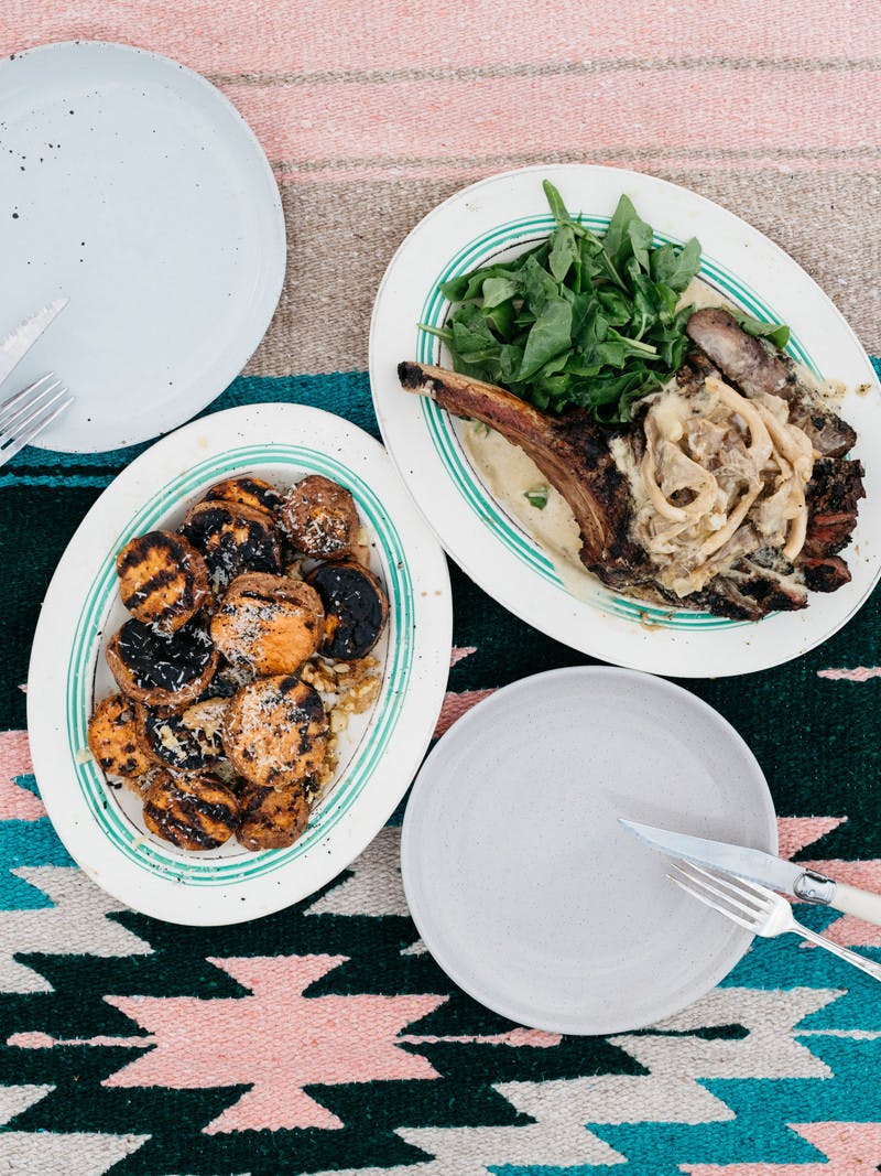 Dishes on a table holding a tomahawk steak topped with onions and cheesy sweet potato rounds.