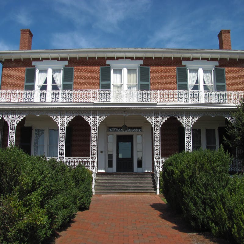 Ware-Lyndon House in Athens, Georgia, brick building with white cast iron trim, large windows, and green shutters, surrounded by bushes.