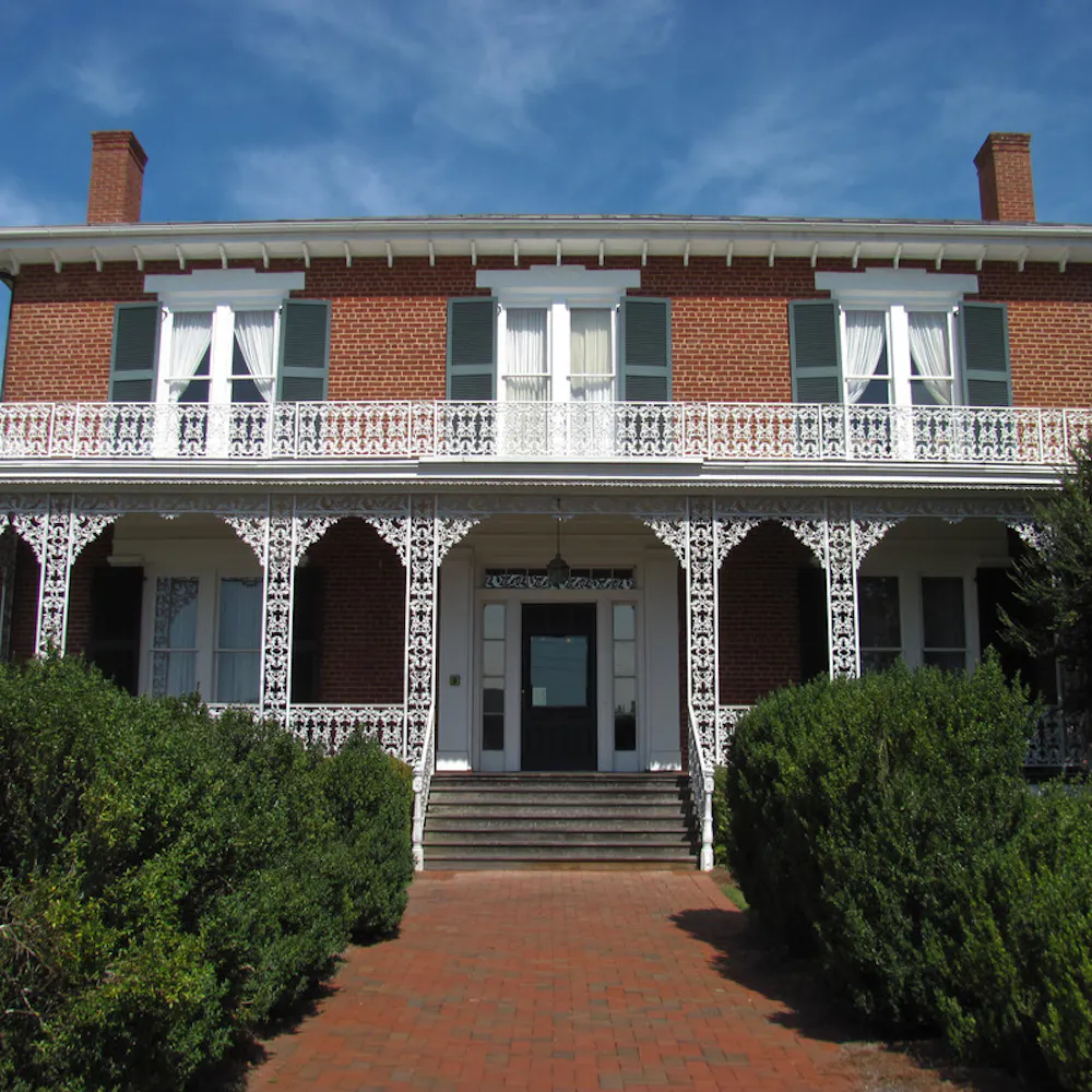 Ware-Lyndon House in Athens, Georgia, brick building with white cast iron trim, large windows, and green shutters, surrounded by bushes.
