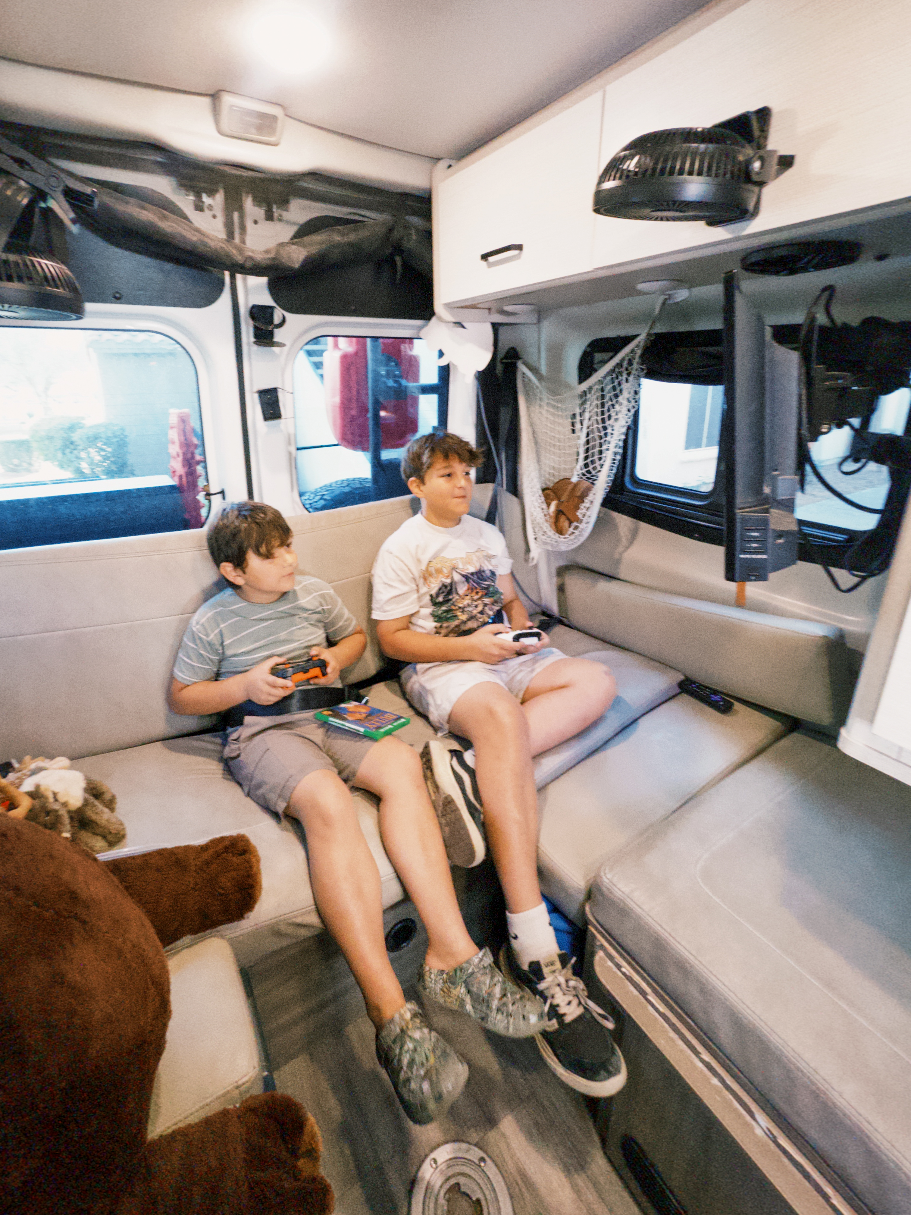 Two young boys playing video games while sitting on the couch inside of a camper van