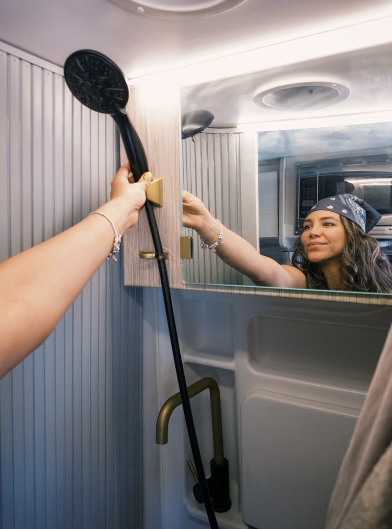 Sara Arango reaching for the showerhead inside of the wet bath in their camper van