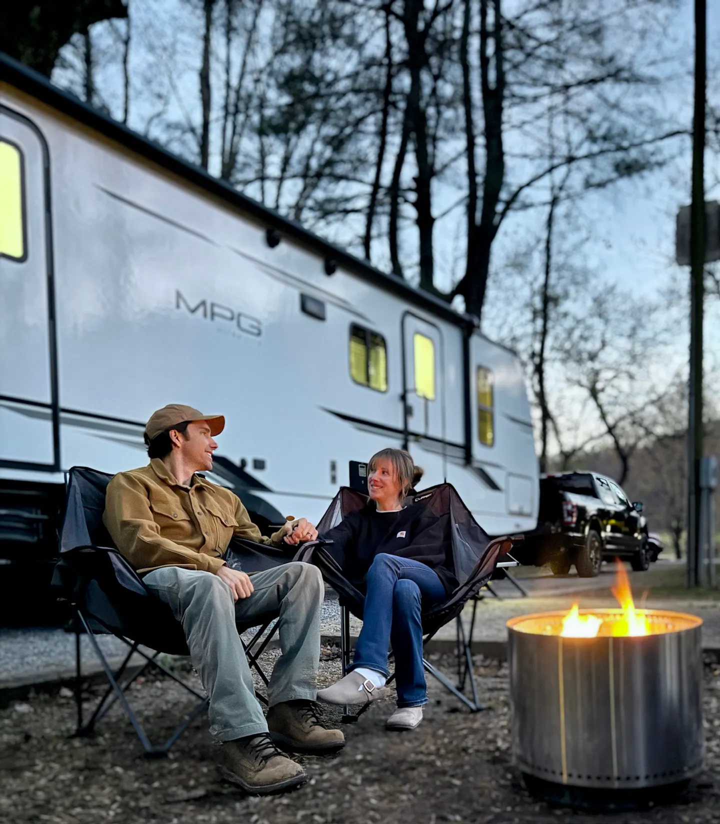 John King and his wife sitting in camp chairs enjoying a campfire outside of their Cruiser MPG travel trailer 