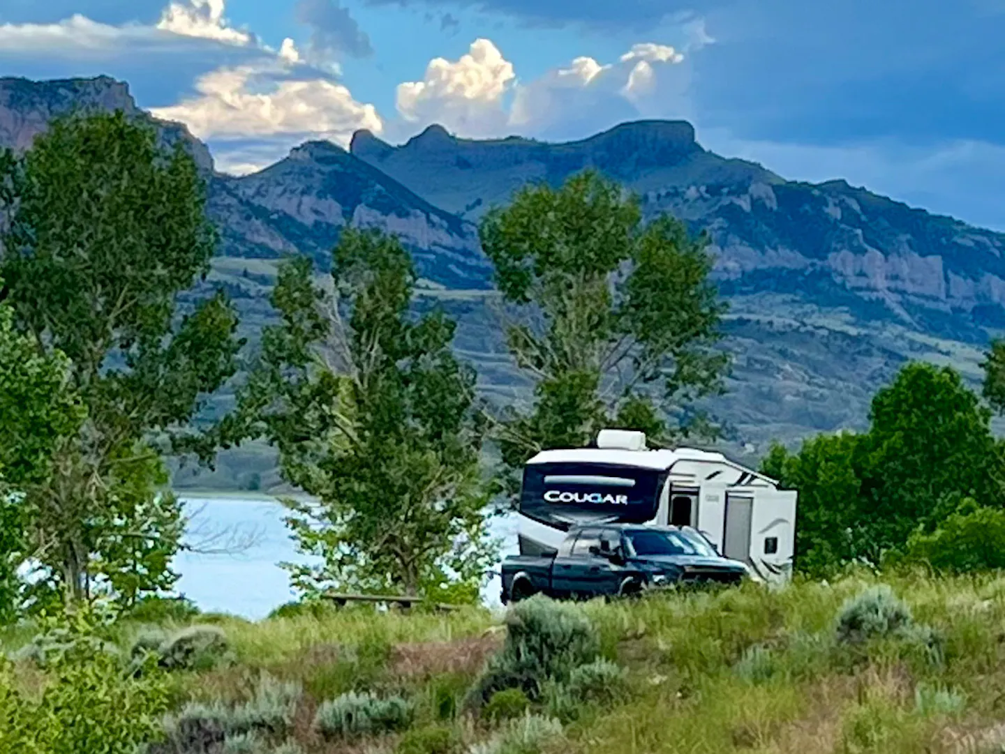 A Keystone Cougar pulled over next to a lake with a mountain backdrop 
