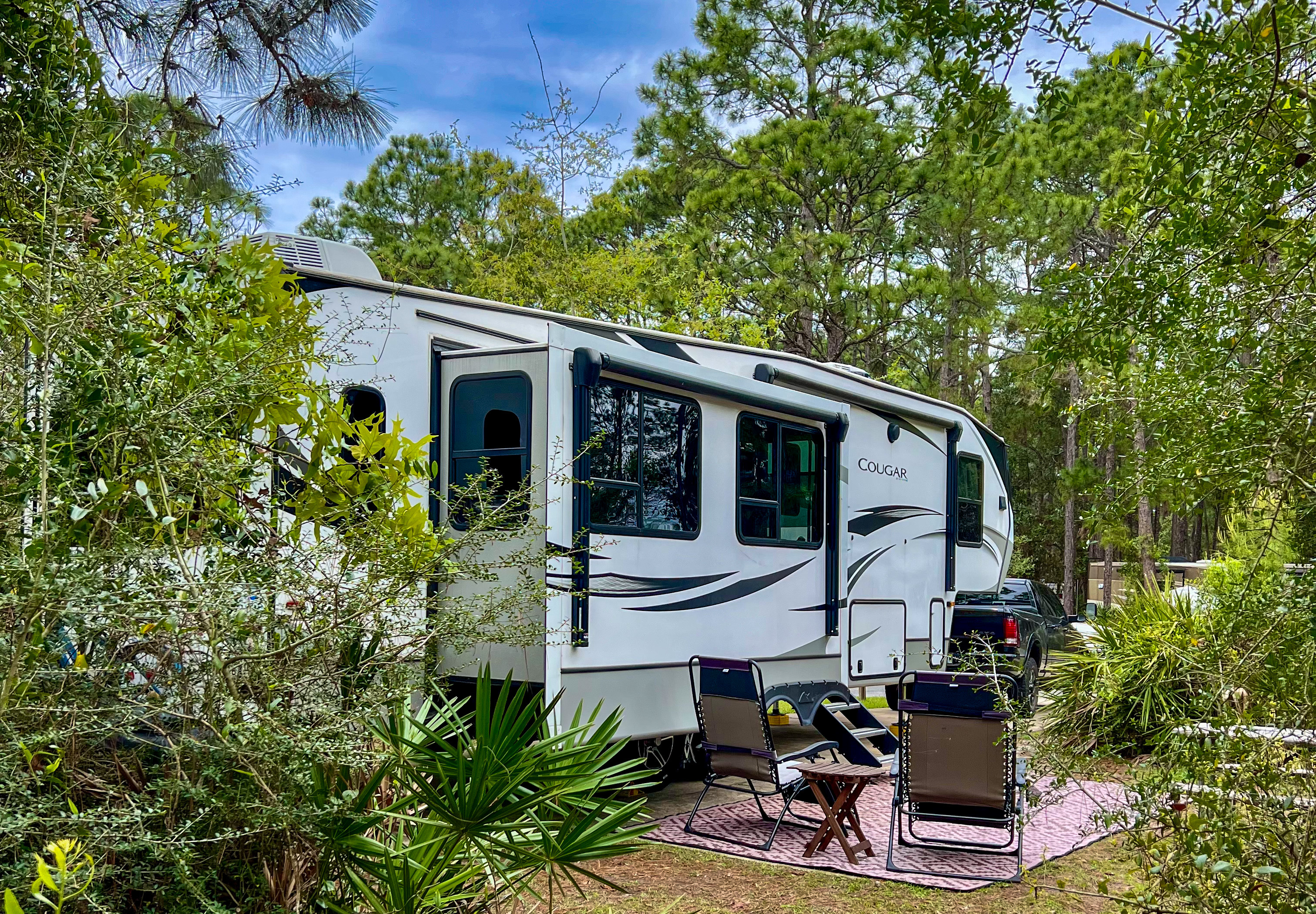A Keystone Cougar fifth wheel tucked into a capsite surrounded by beautiful green foliage 