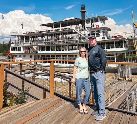 A man and woman standing in front of a riverboat