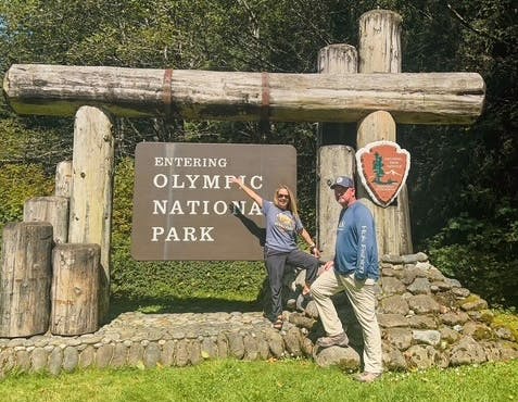 A man and woman standing in front of the entrance to Olympic National Park 