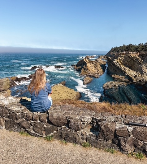 A woman sitting on a rocky ledge toward the ocean