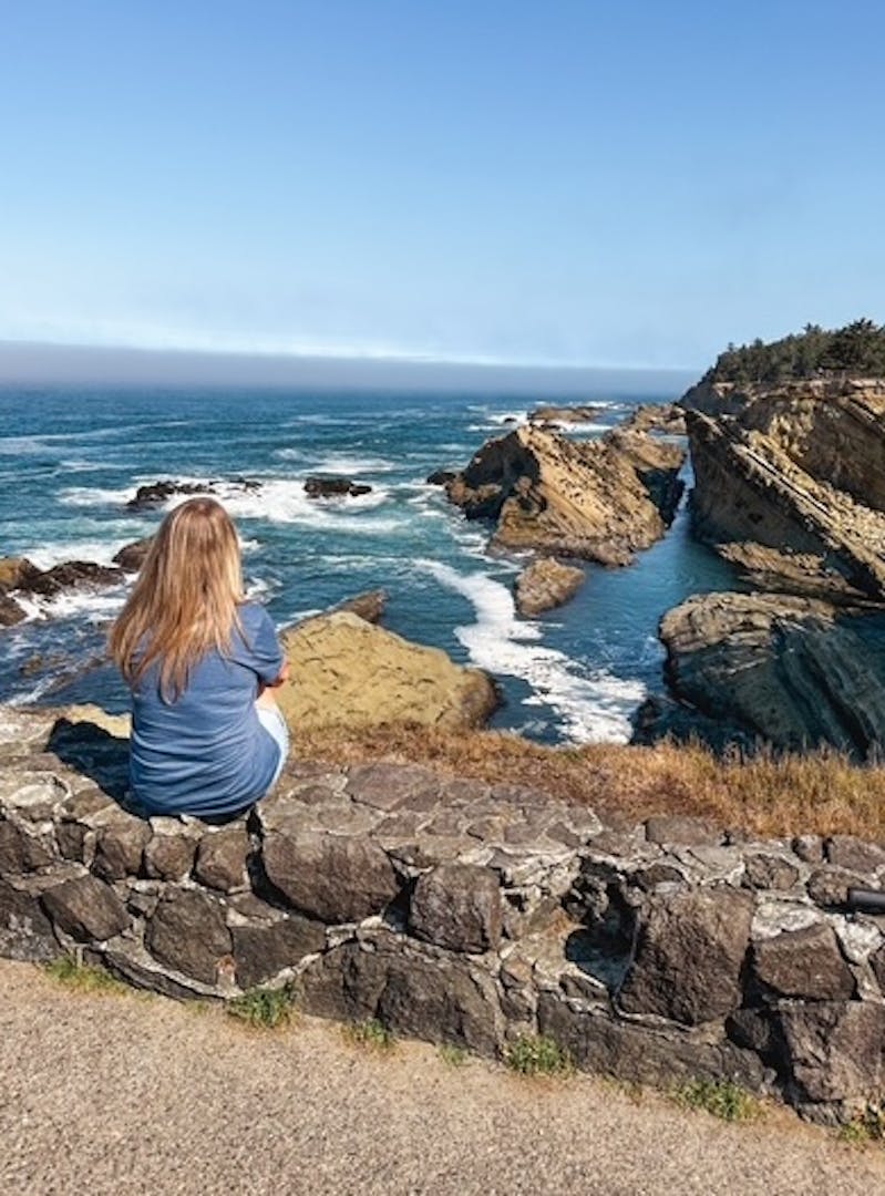A woman sitting on a rocky ledge toward the ocean