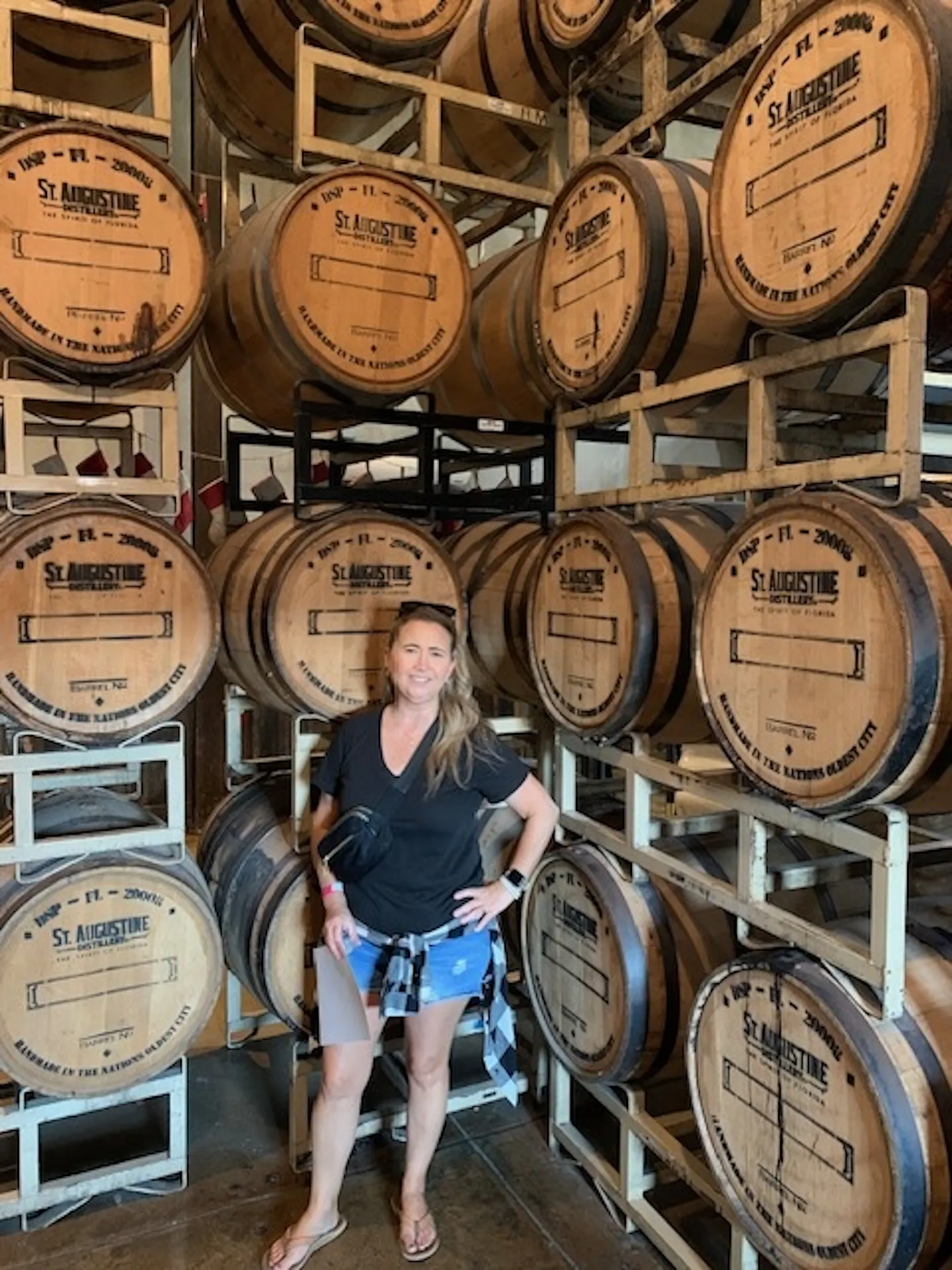 A woman standing in front of whisky barrels at a distillery 