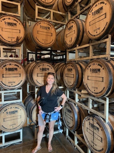 A woman standing in front of whisky barrels at a distillery 