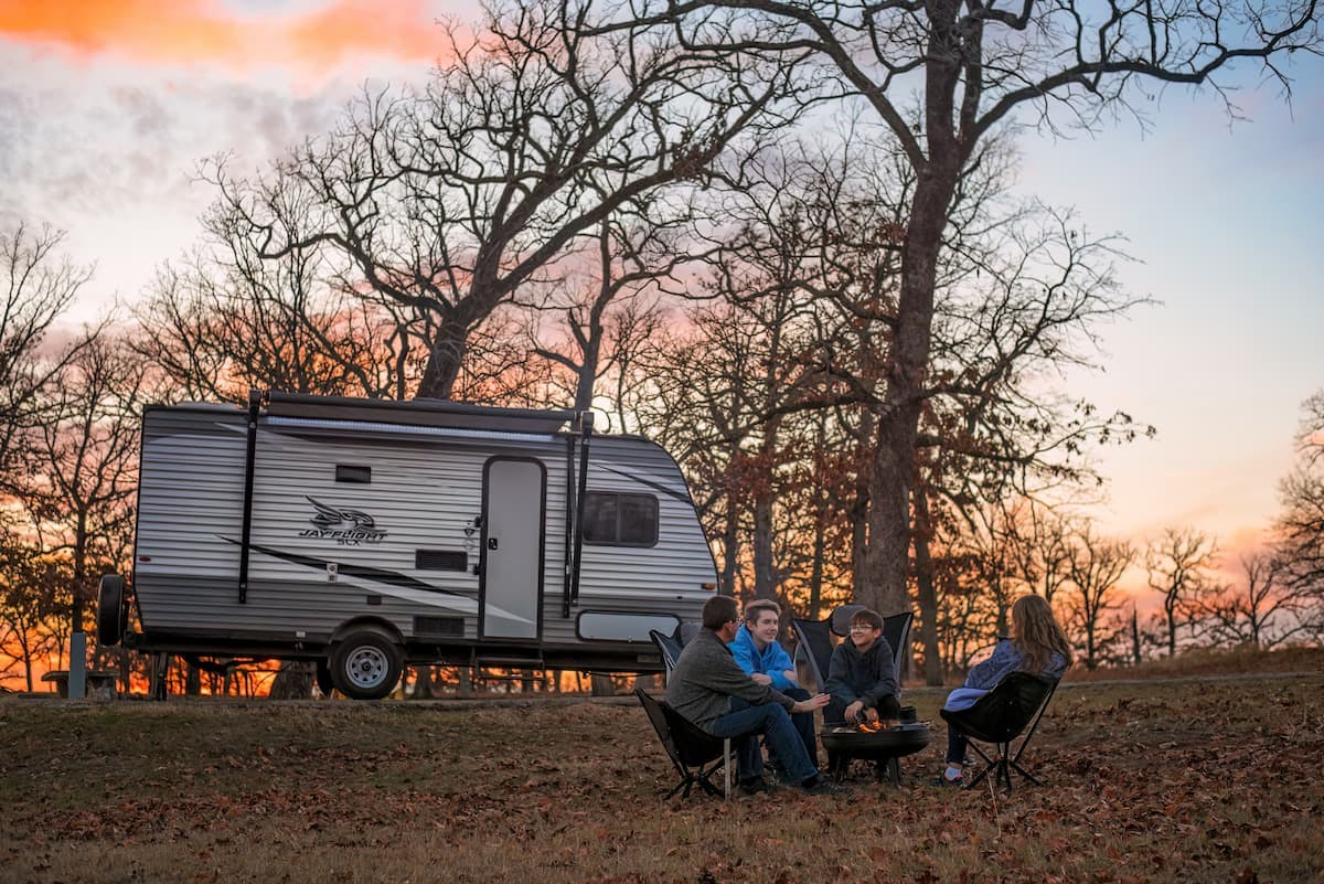 The Jason and Alison Takacs family gather around a campfire next to their Jayco Jay Flight travel trailer during sunset.