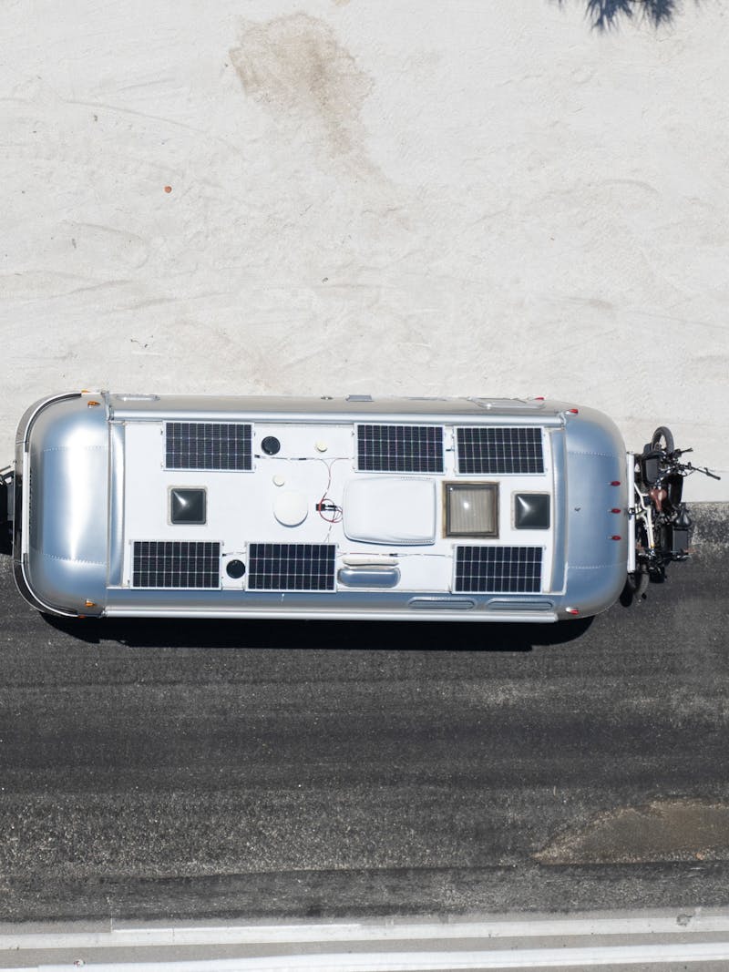 An Airstream hitched to a truck with solar panels on both roofs pulled over to the side of a sandy road.