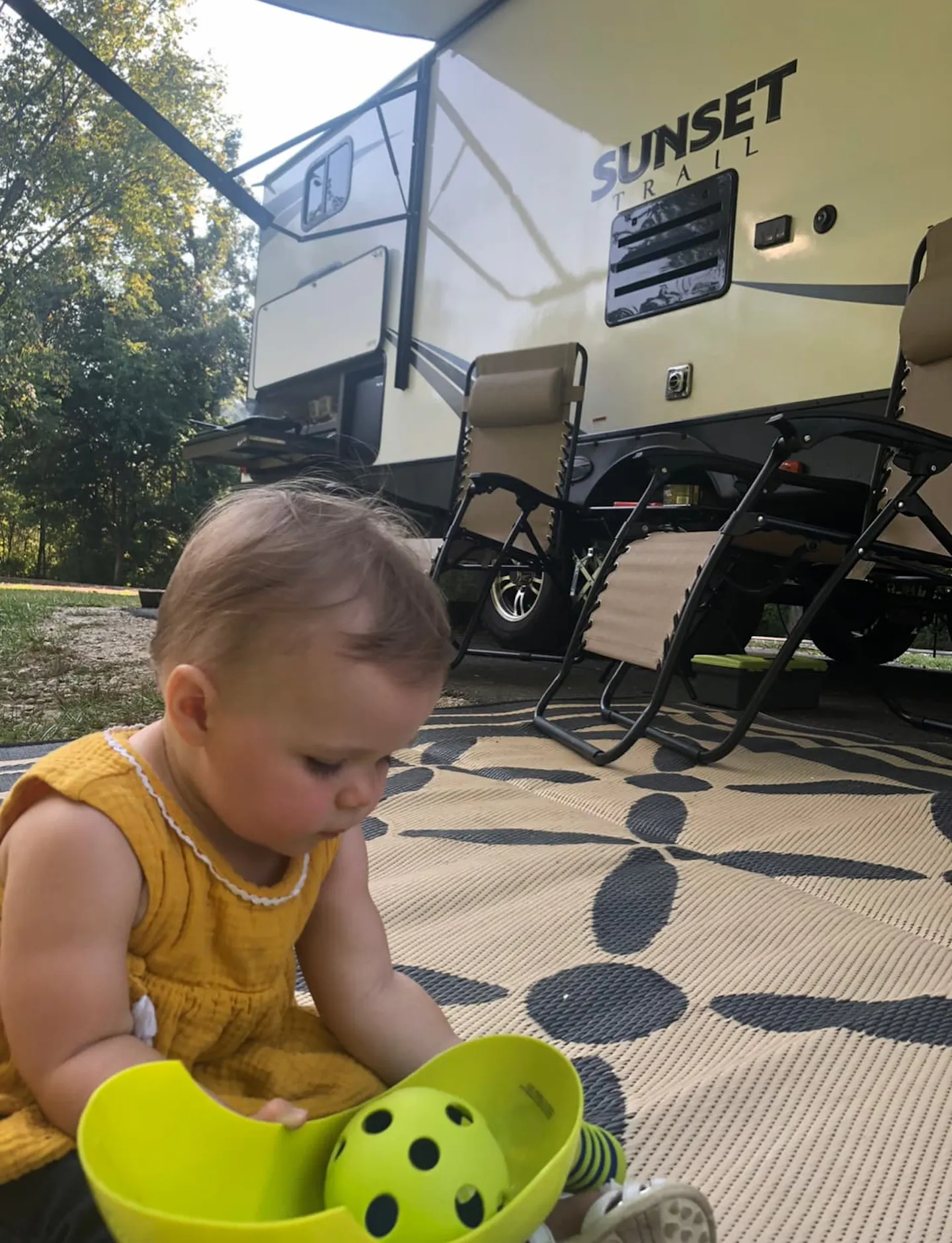 A baby playing on the ground outside an RV.