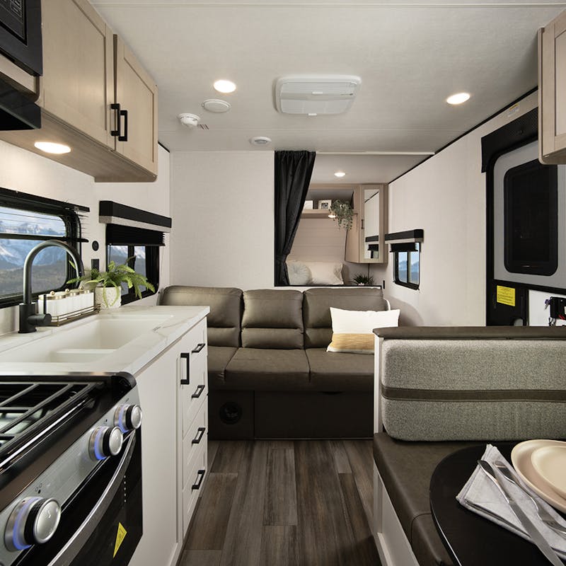 A kitchen and living room view of a Open Range Colt travel trailer with mountain views out the windows.