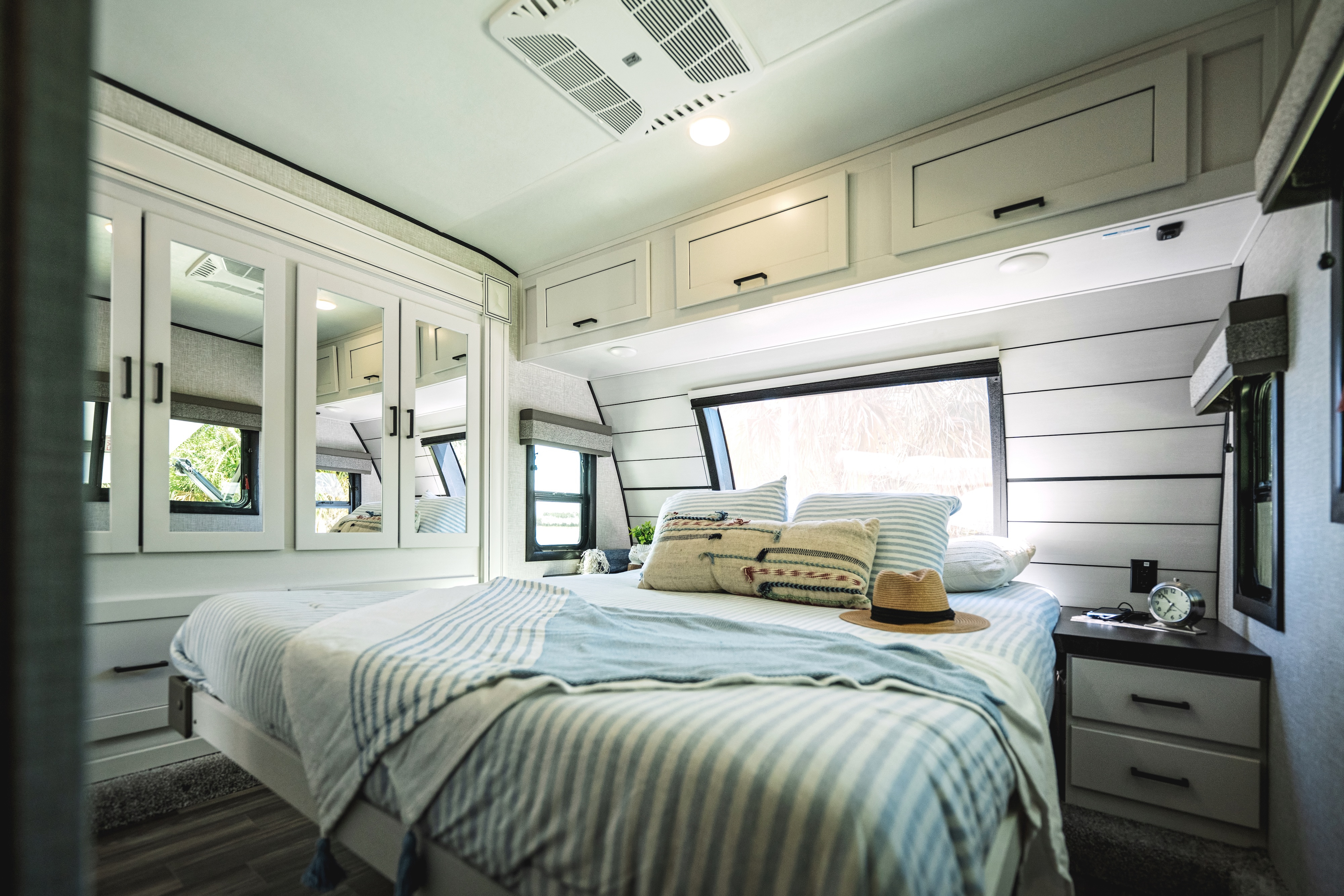 A king sized bed inside of a Starcraft fifth wheel decorated in a beachy, coastal theme. 
