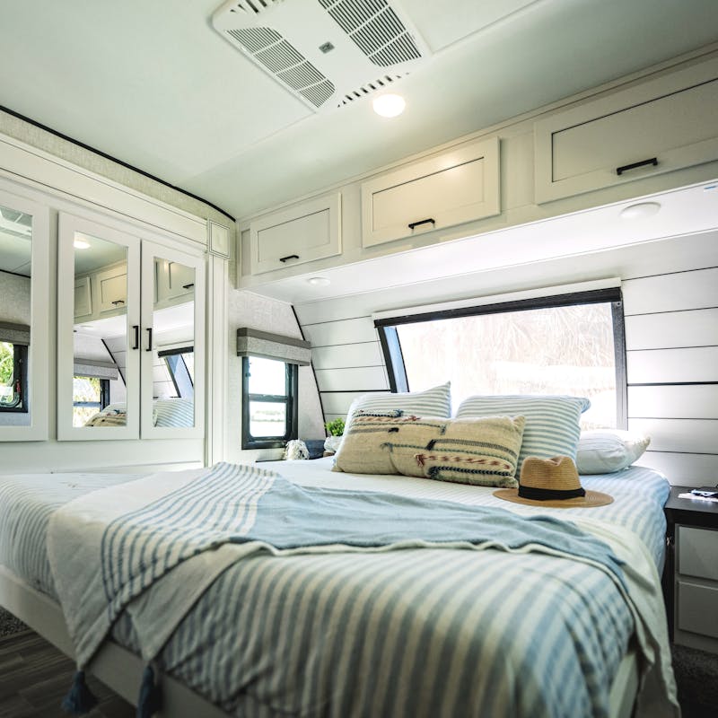 A king sized bed inside of a Starcraft fifth wheel decorated in a beachy, coastal theme.