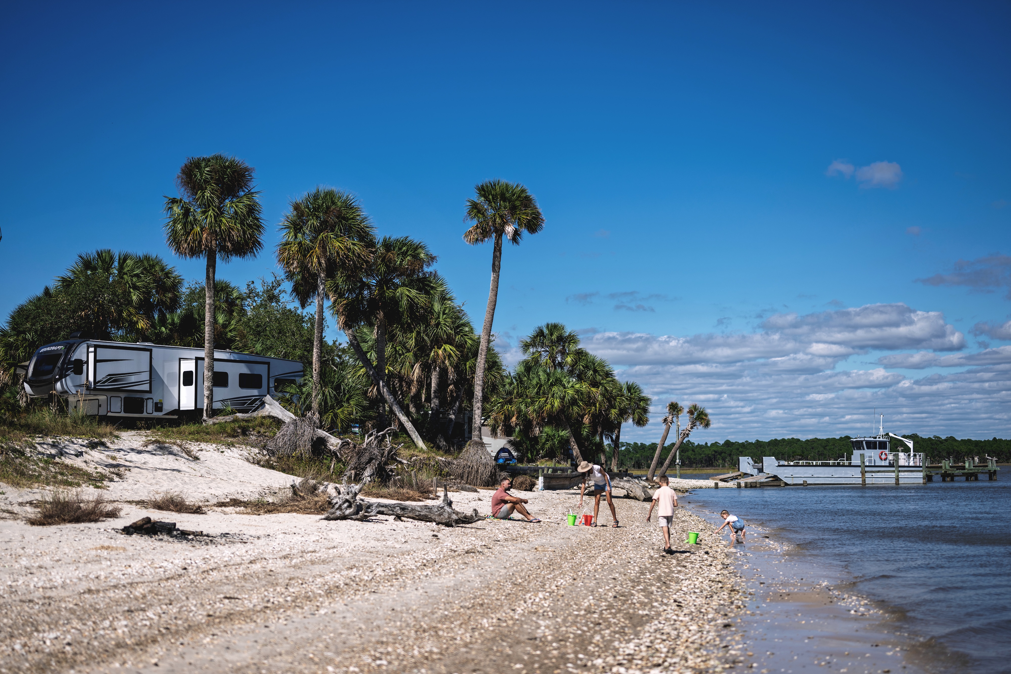 A family plays in the sand with toy buckets and shovels on a beach where their RV is parked.