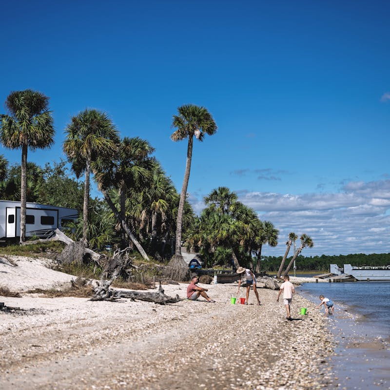 A family plays in the sand with toy buckets and shovels on a beach where their RV is parked.