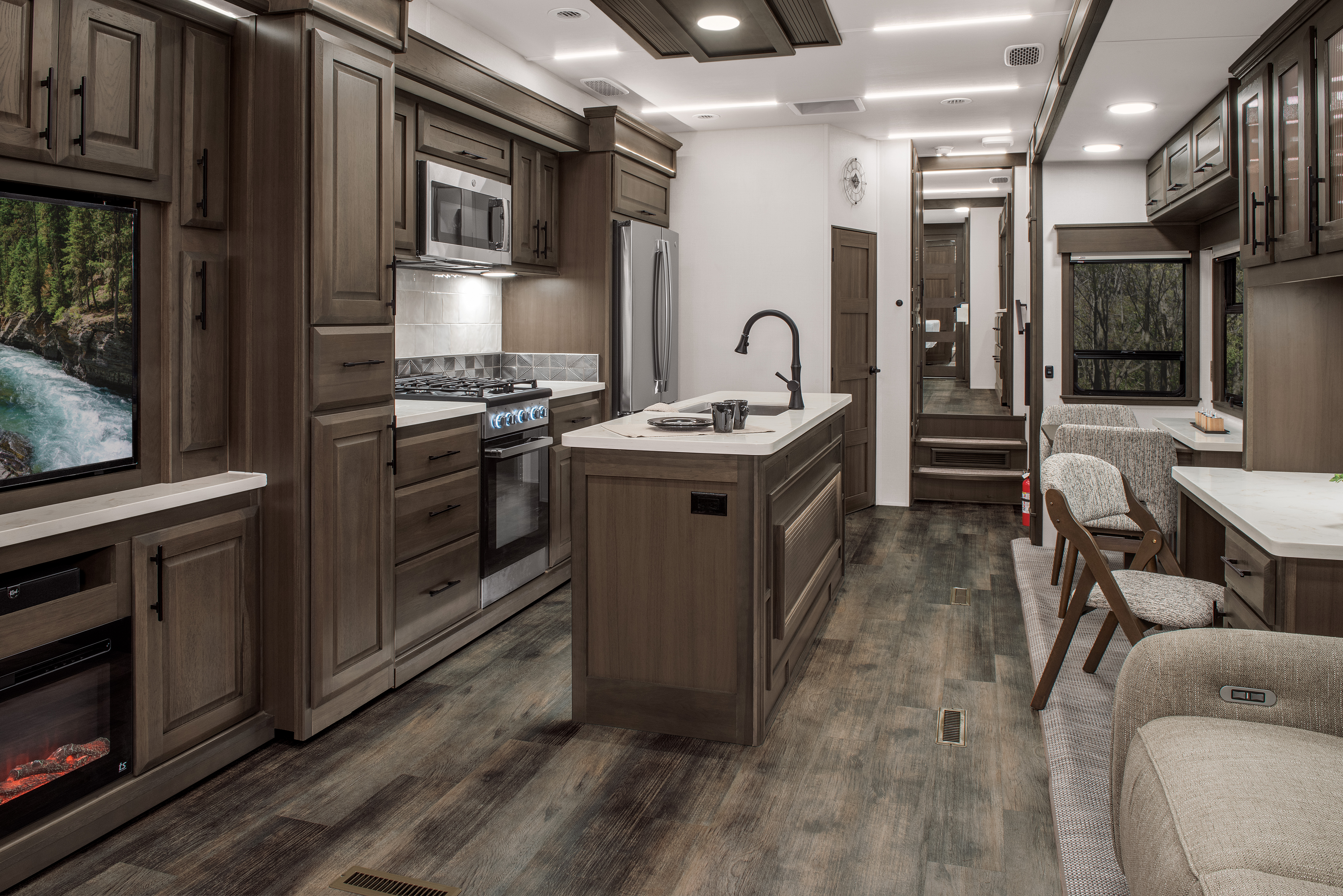 The living and kitchen area of a DRV Mobile Suites fifth wheel with dark wood features and white marble countertops. 