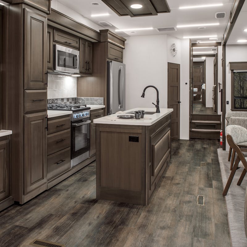 The living and kitchen area of a DRV Mobile Suites fifth wheel with dark wood features and white marble countertops.