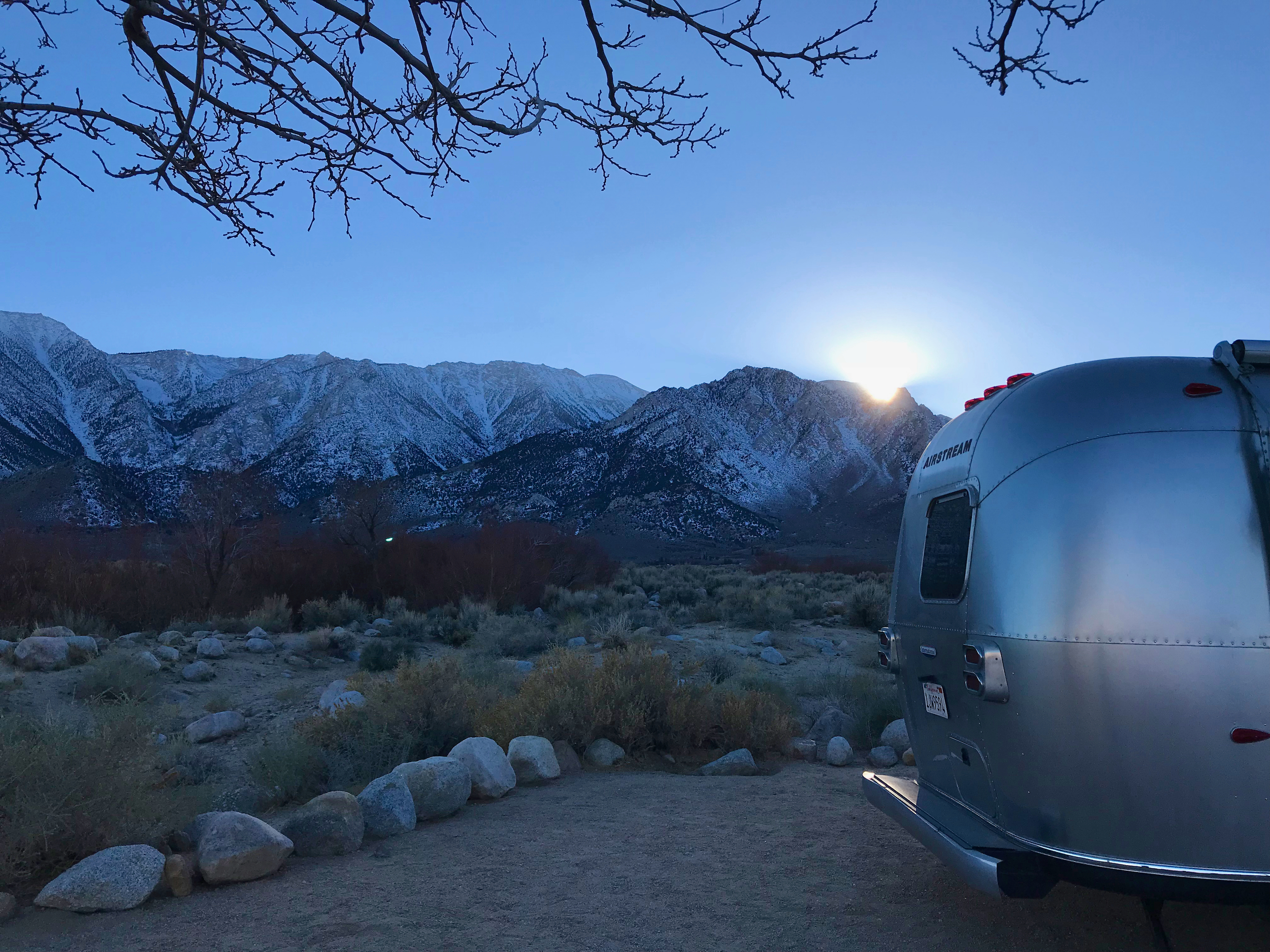 Dr. Na's Airstream parked at a campsite with snow capped mountains in the distance. 