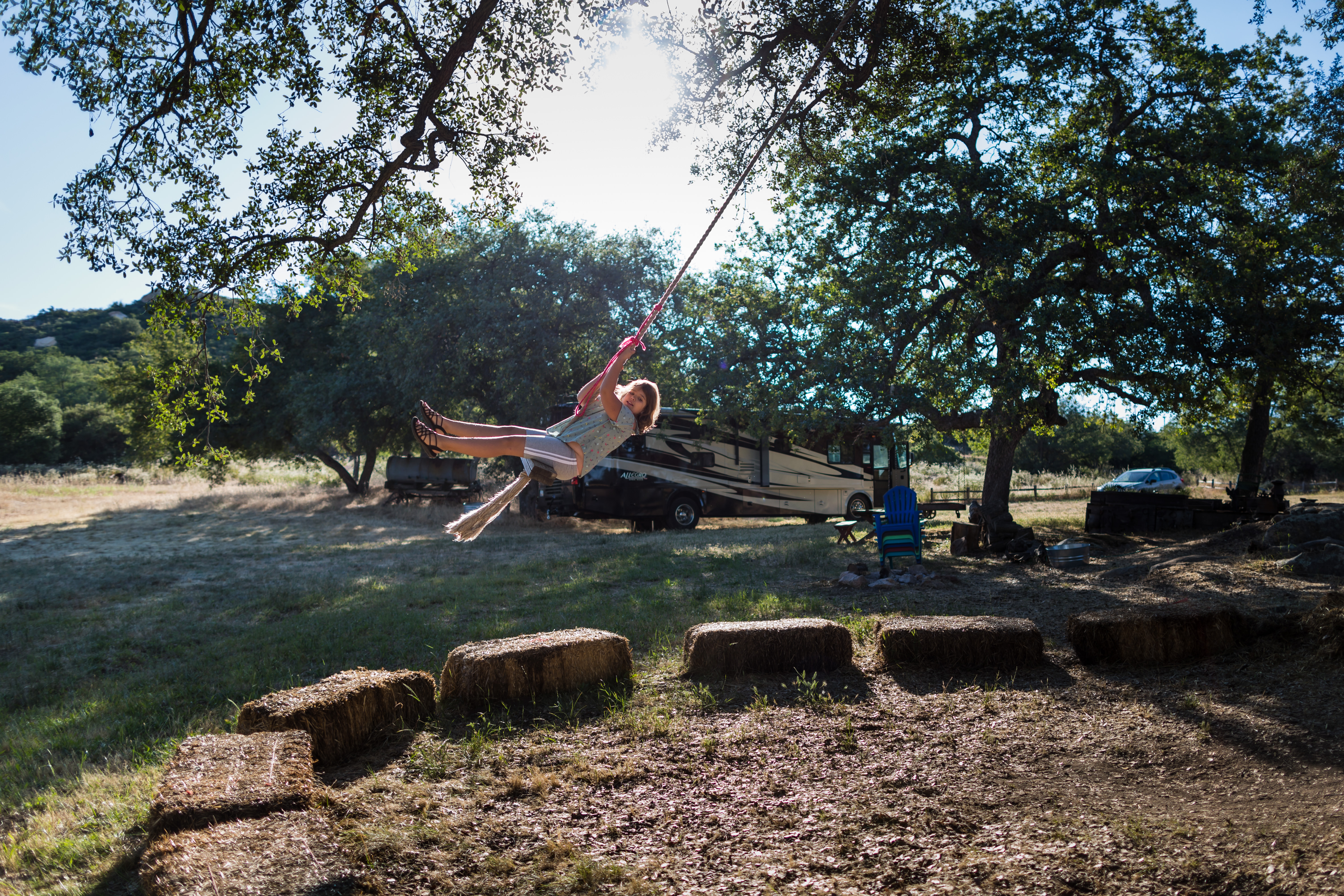 A child swings from a rope swing with an Allegro class A RV in the background.