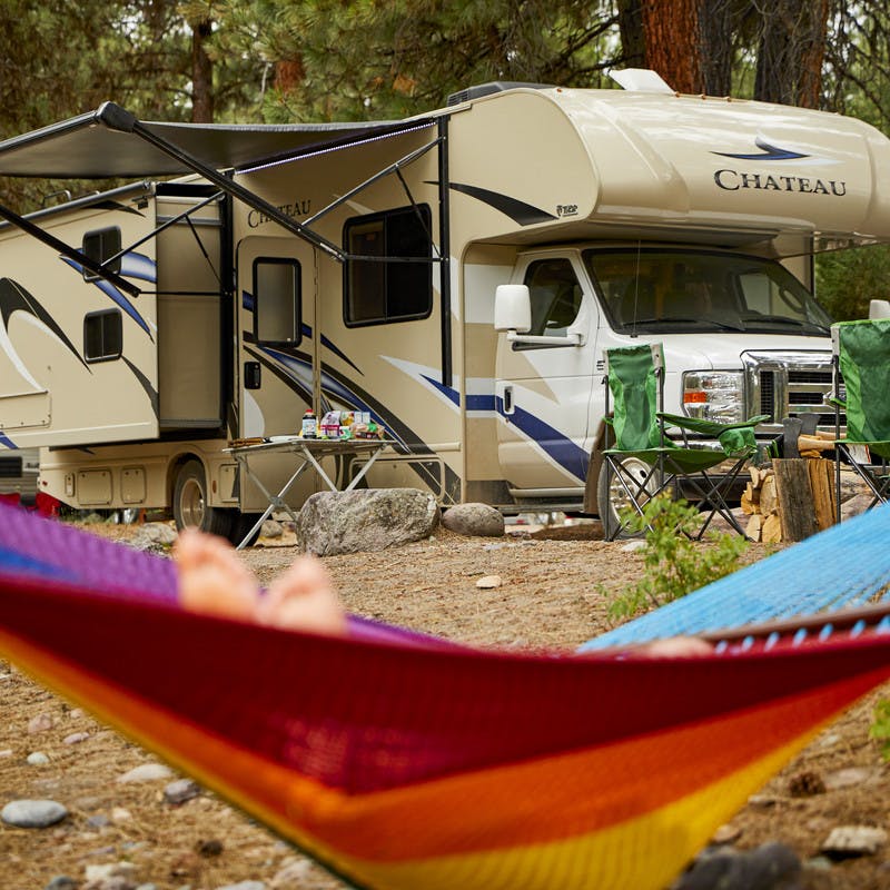 A participants relaxes in a rainbow hammock in front of a Thor Motor Coach Class C RV.