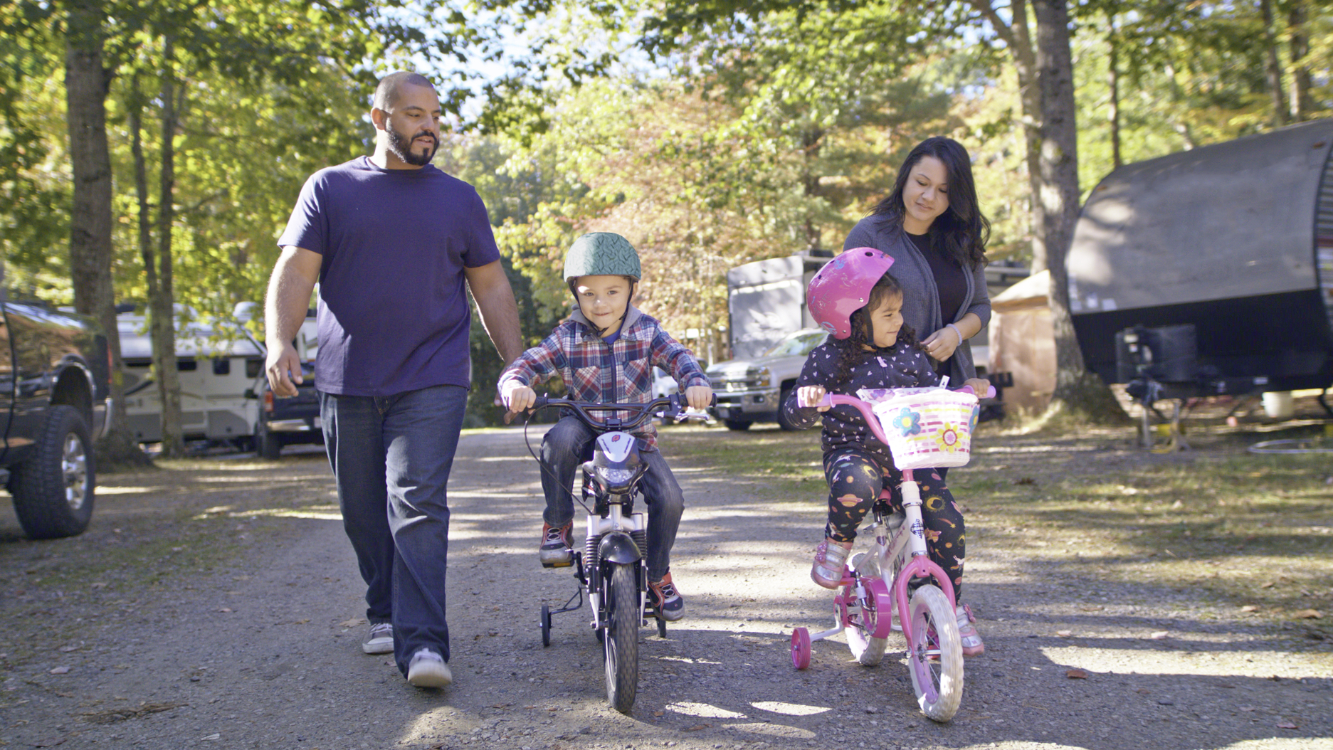 Luis and Sandra walking alongside their kids riding bikes through an RV campground. 
