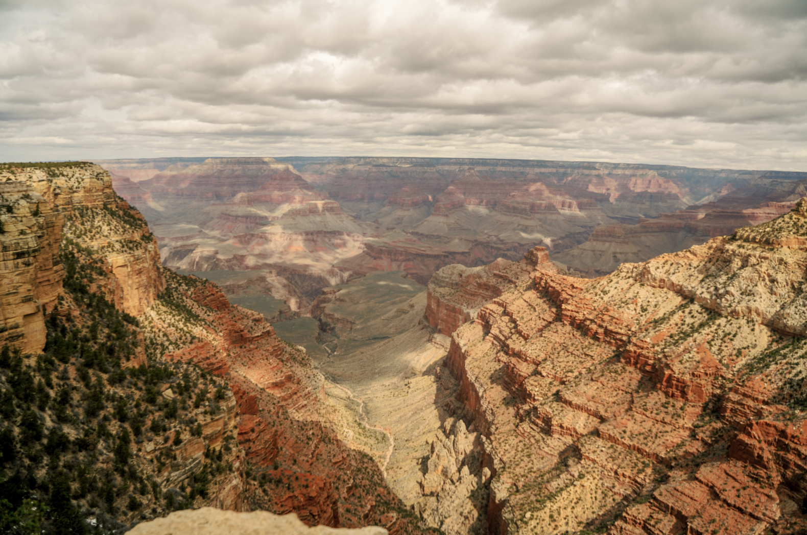 View looking out over the South Rim of Grand Canyon with lots of layered red rock and cloudy skies
