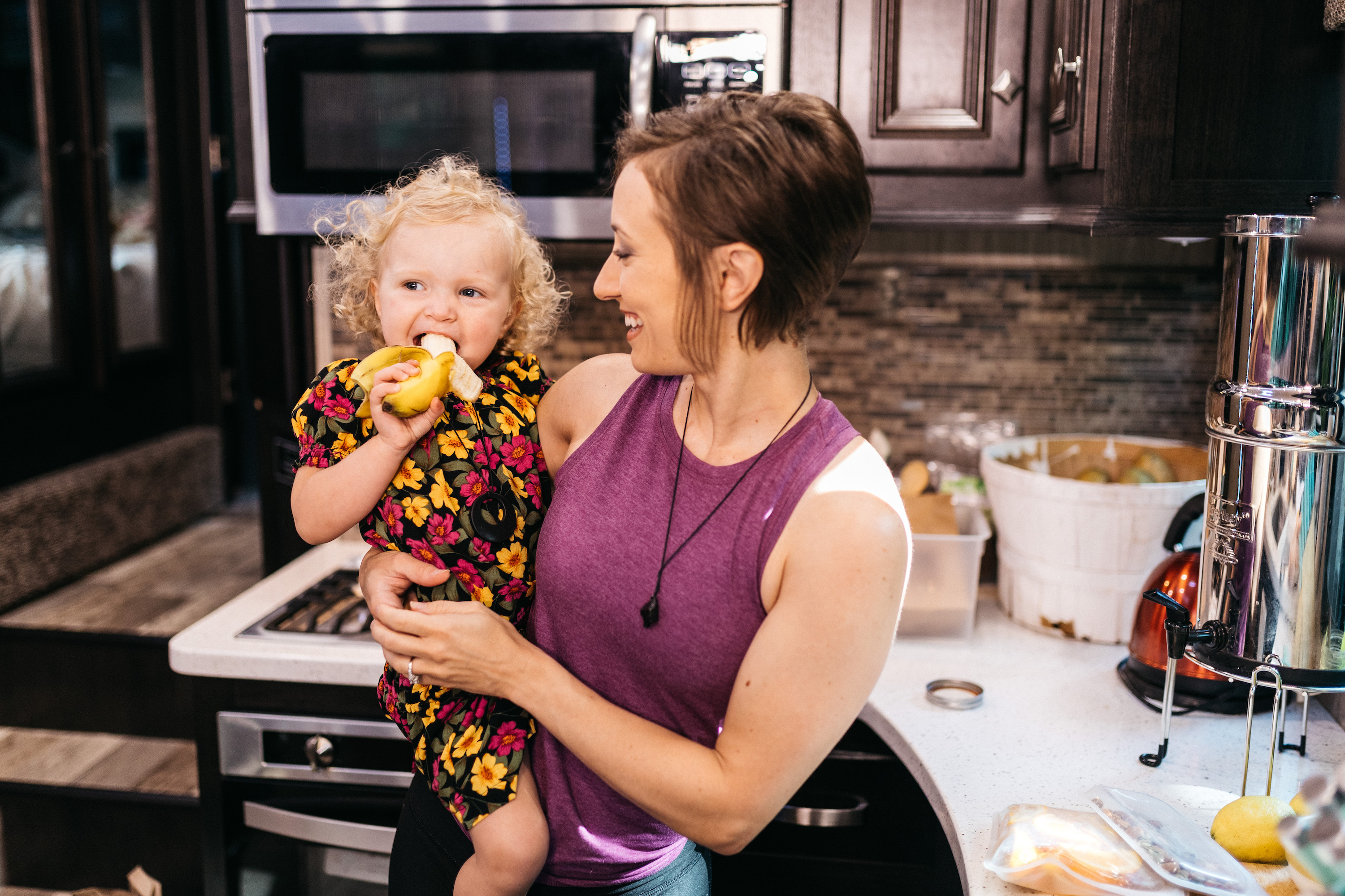 A woman holds a young girl who is happily eating a banana. 