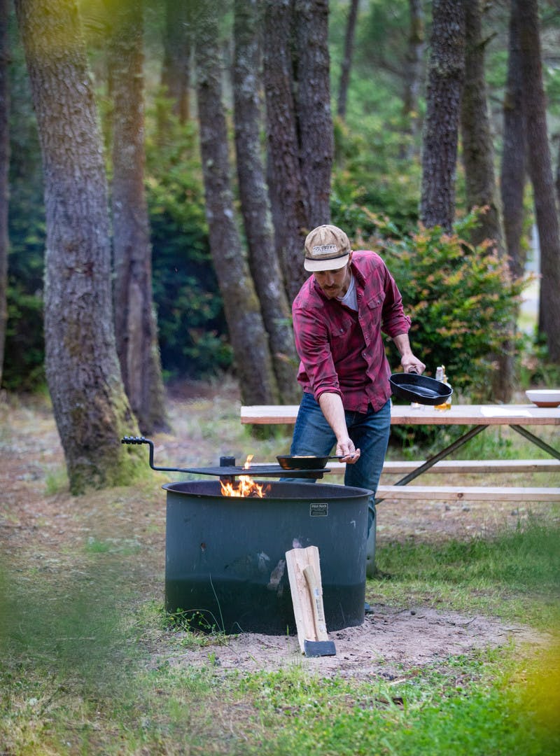 Man in a plaid shirt wearing a hat, cooking the bananas foster in a cast iron over a campfire.