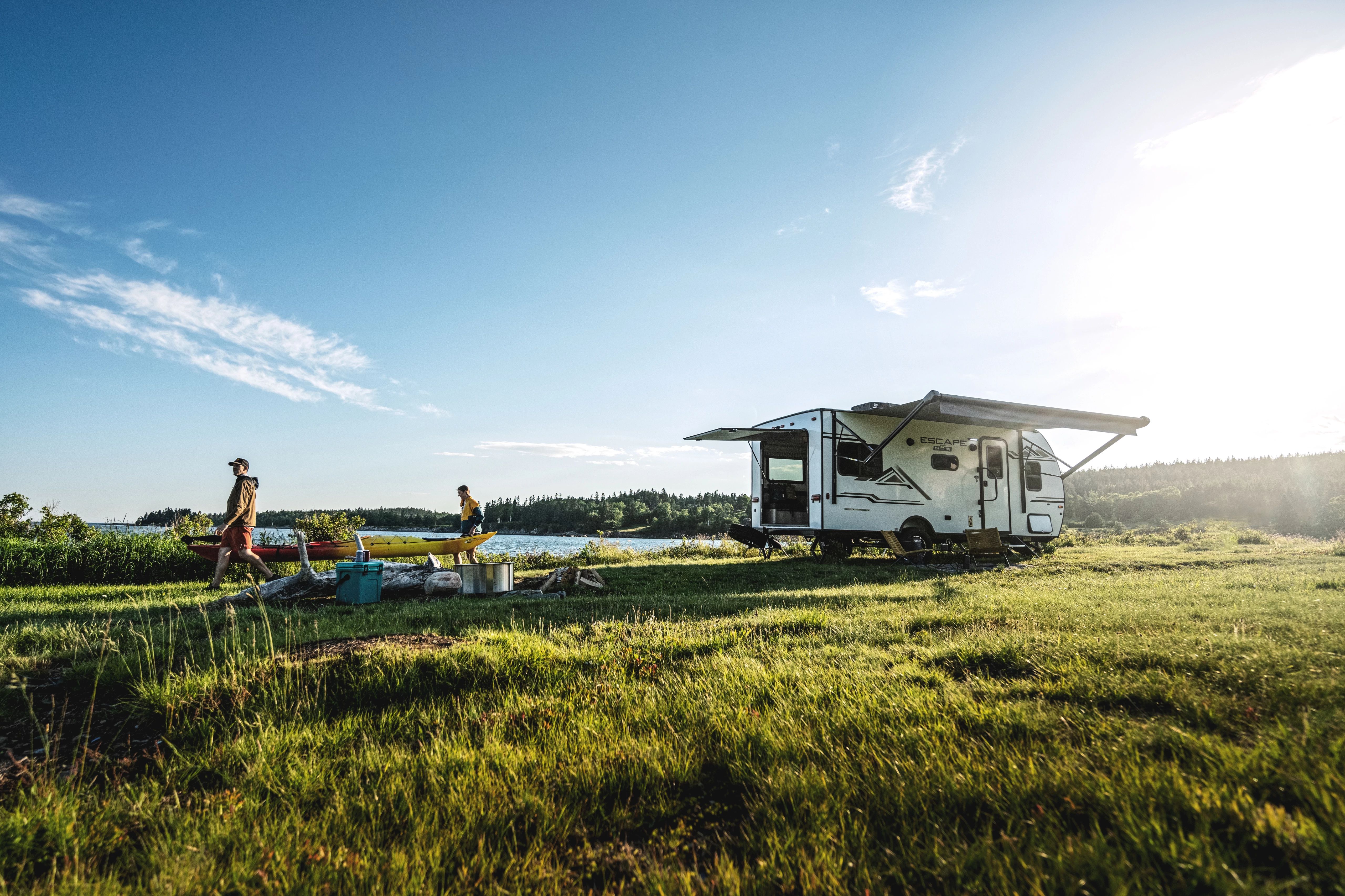 A couple walking away from a small travel trailer holding a kayak