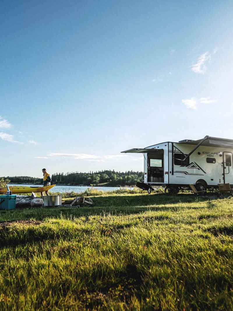 A couple walking away from a small travel trailer holding a kayak