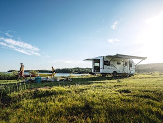 A couple walking away from a small travel trailer holding a kayak