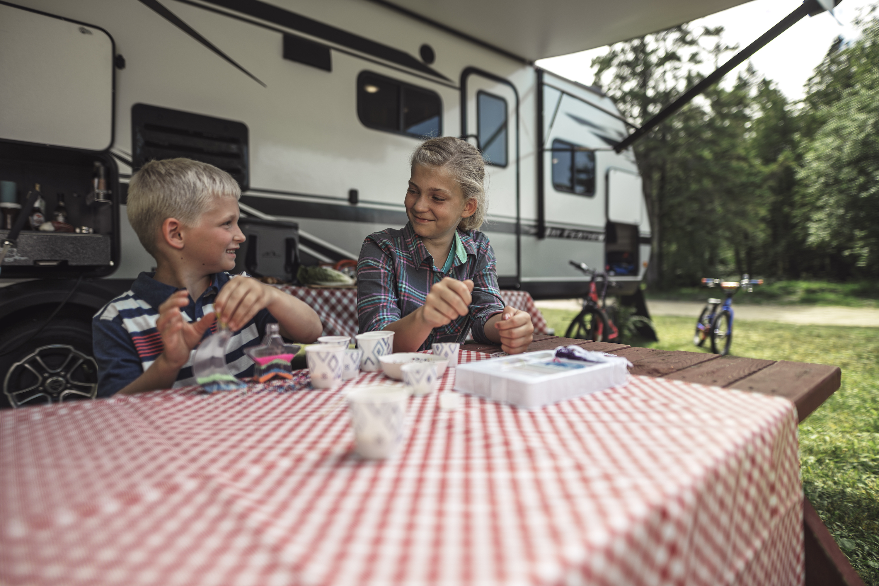 two kids sit at a picnic table at a campsite by an RV