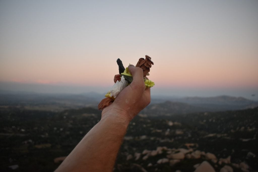 Hand holding trash in front of sunset over mountain range