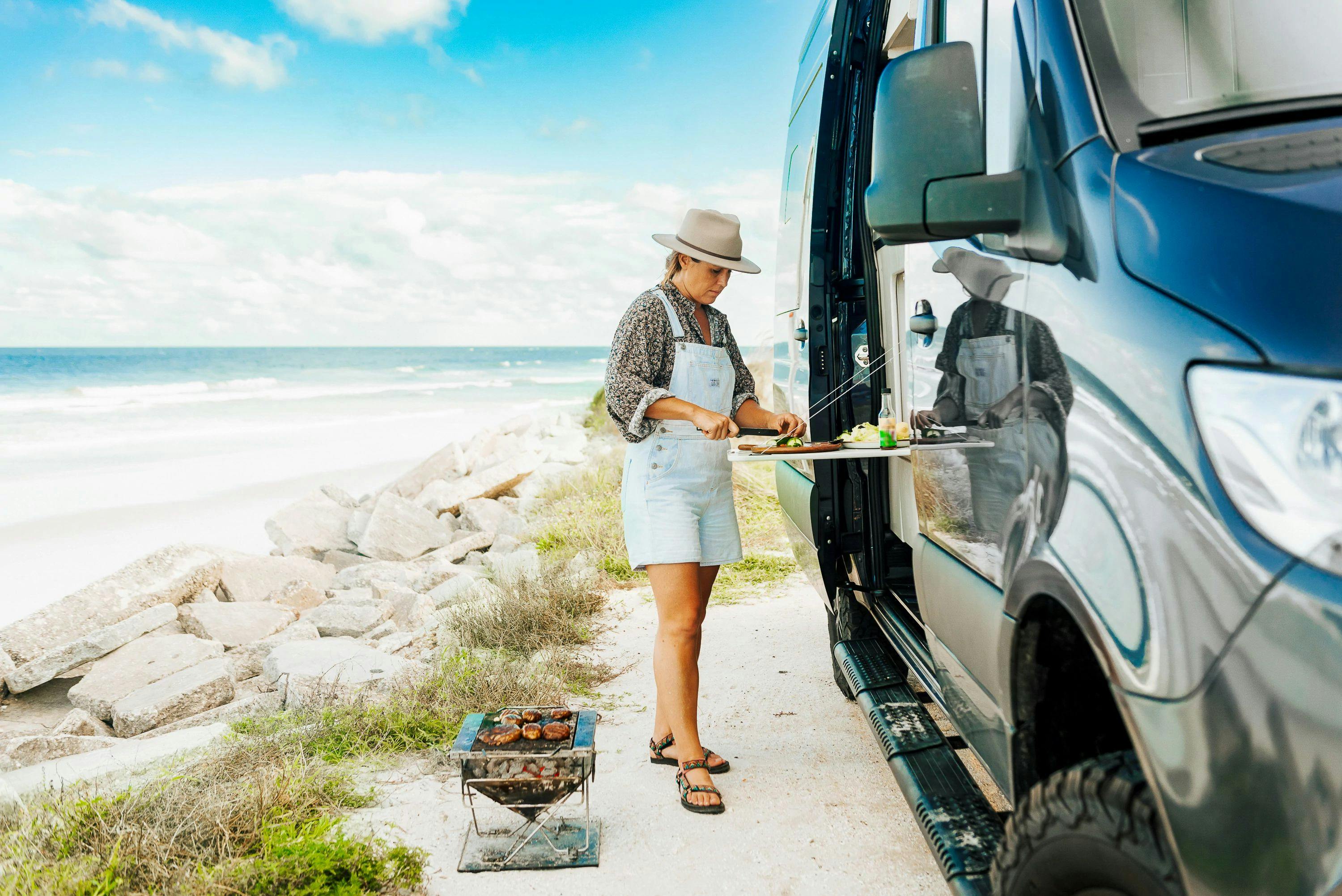 Sarah Glover prepares mushroom noodle salad on the drop down table on the side of a TMC Tranquility camper van