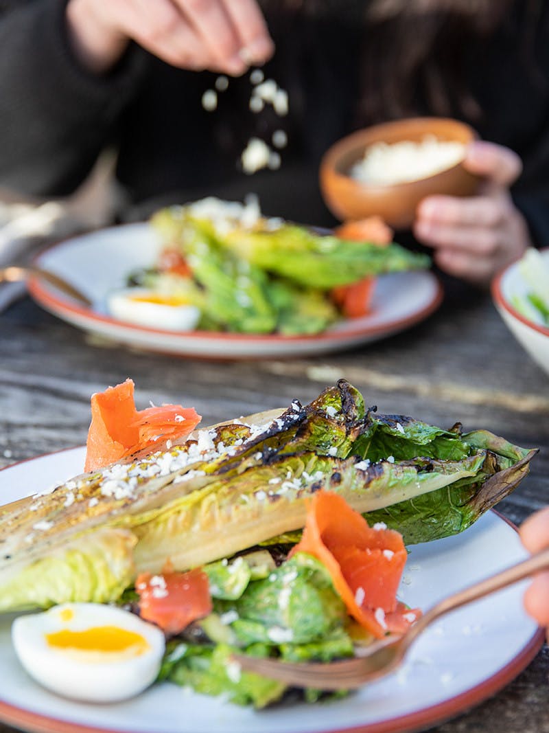 Caesar salad with grilled asparagus, soft-boiled egg, and lox on a plate while man holds fork about to eat salad.