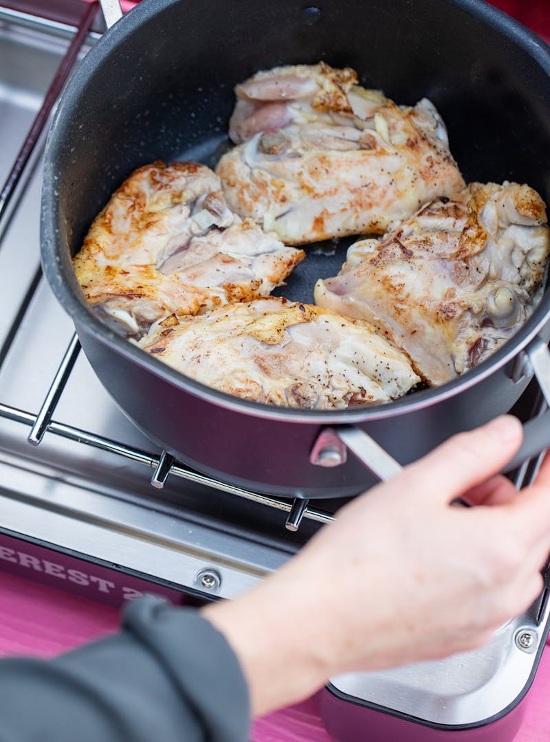 Browning chicken thighs in a pot on a camp stove.