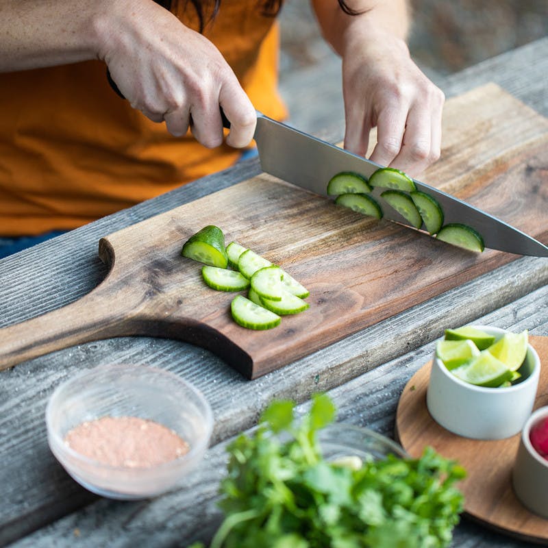 Woman chops cucumber on cutting board with knife.