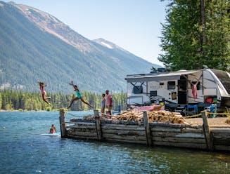 Kids jump off of a dock into a lake next to an RV.