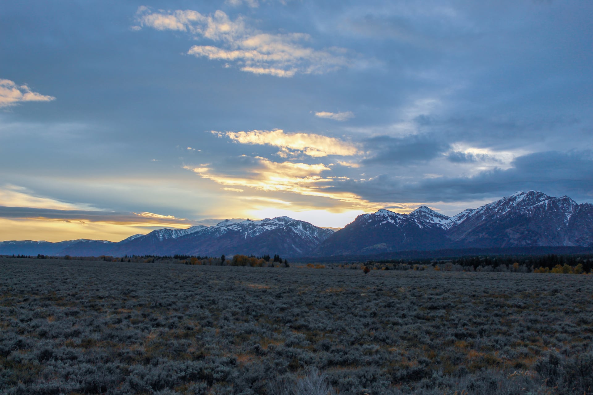 Snowy peaked mountains with grassy field and sunset sky