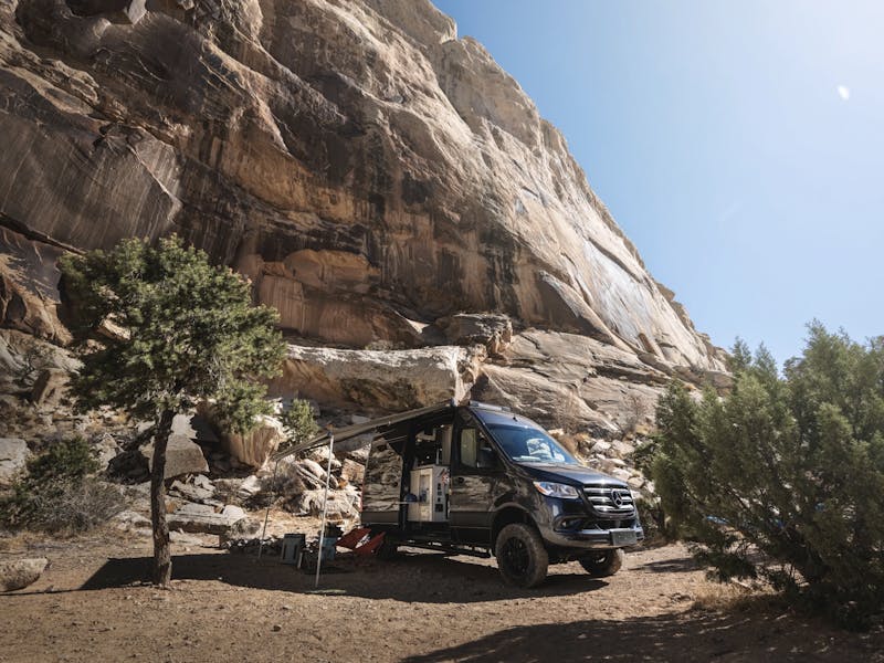 A Thor Motor Coach Sanctuary parked at a campsite next to a rocky mountainside.