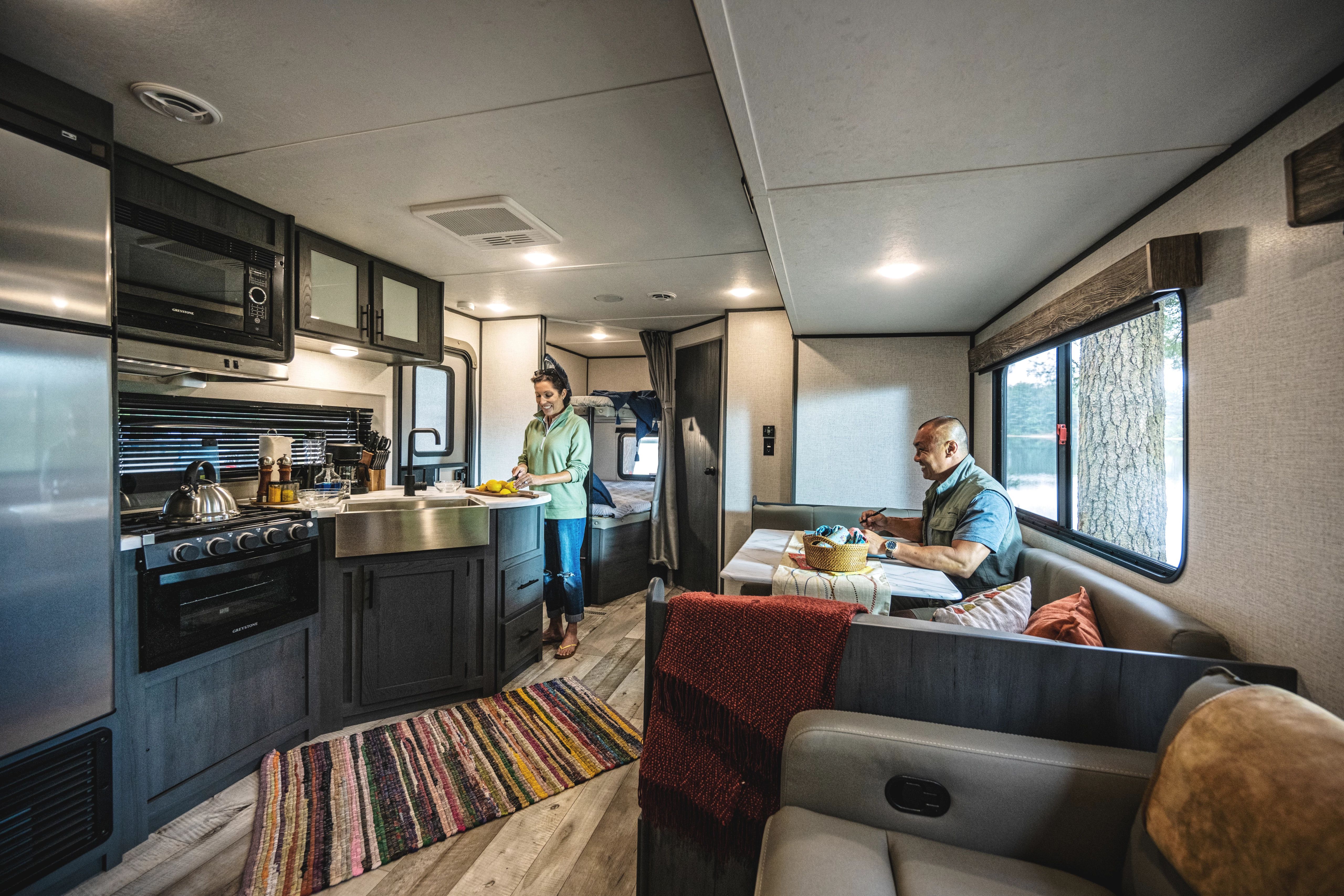 A couple relaxes inside the living are and kitchen of a travel trailer