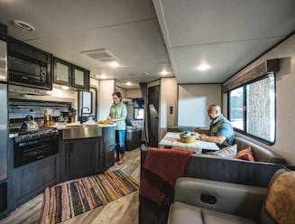 A couple relaxes inside the living are and kitchen of a travel trailer