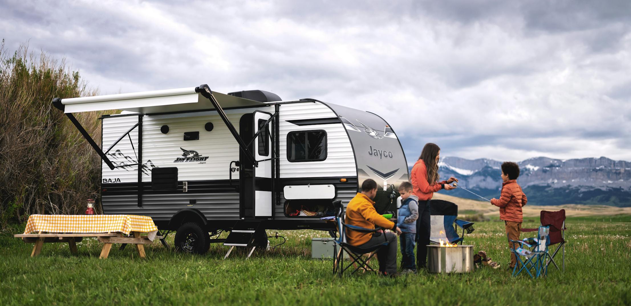 A family gathered around a campfire near a Jayco Jay Flight in a mountain landscape.