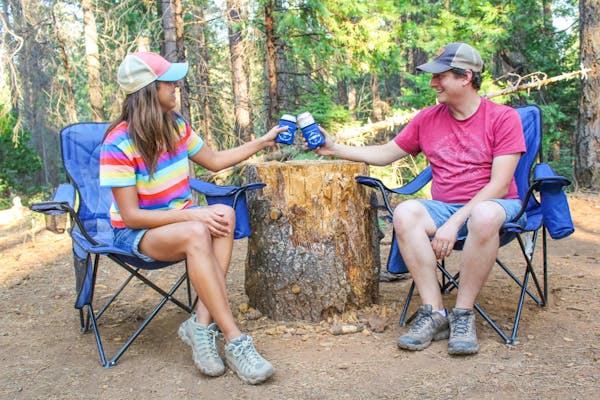 Jesse & Rachael Lyons sitting in camp chairs and cheers each other with drinks in their hands.