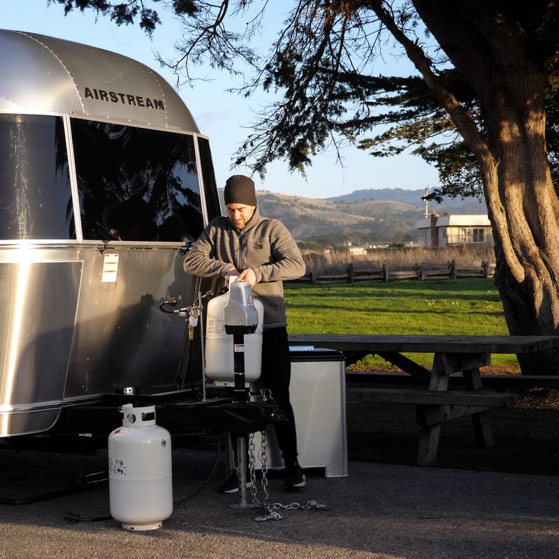 A man standing outside next to his RV holding a propane tank.  