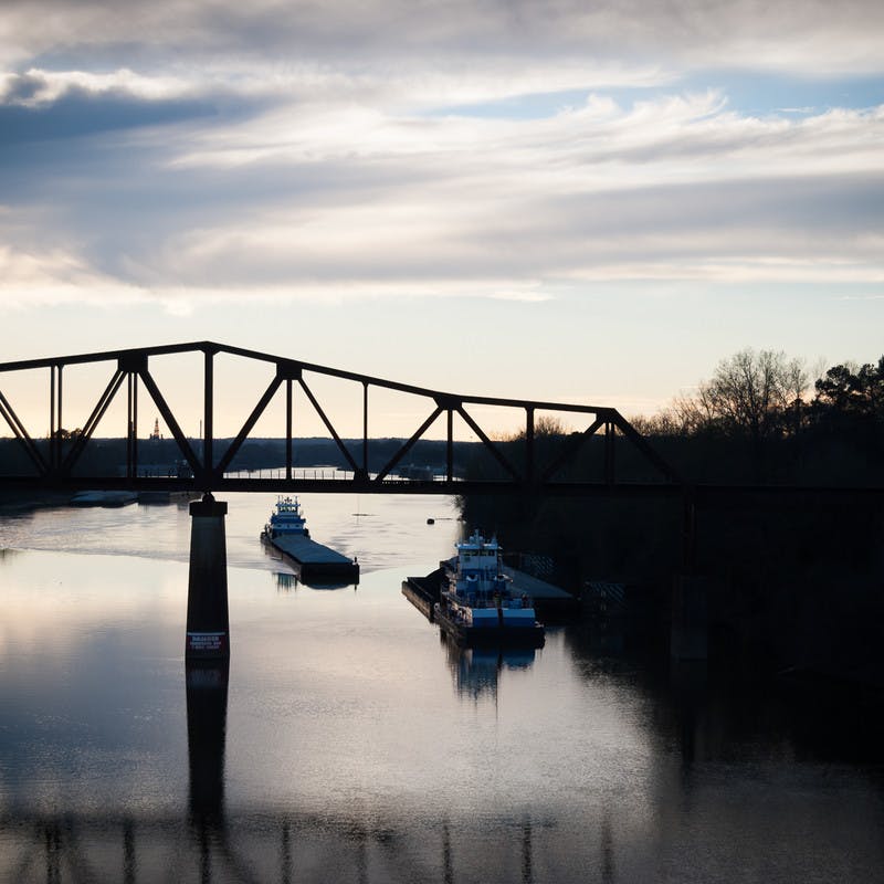 Riverwalk near University of Alabama in Tuscaloosa, Alabama, at sunset with a bridge and boats on the water.